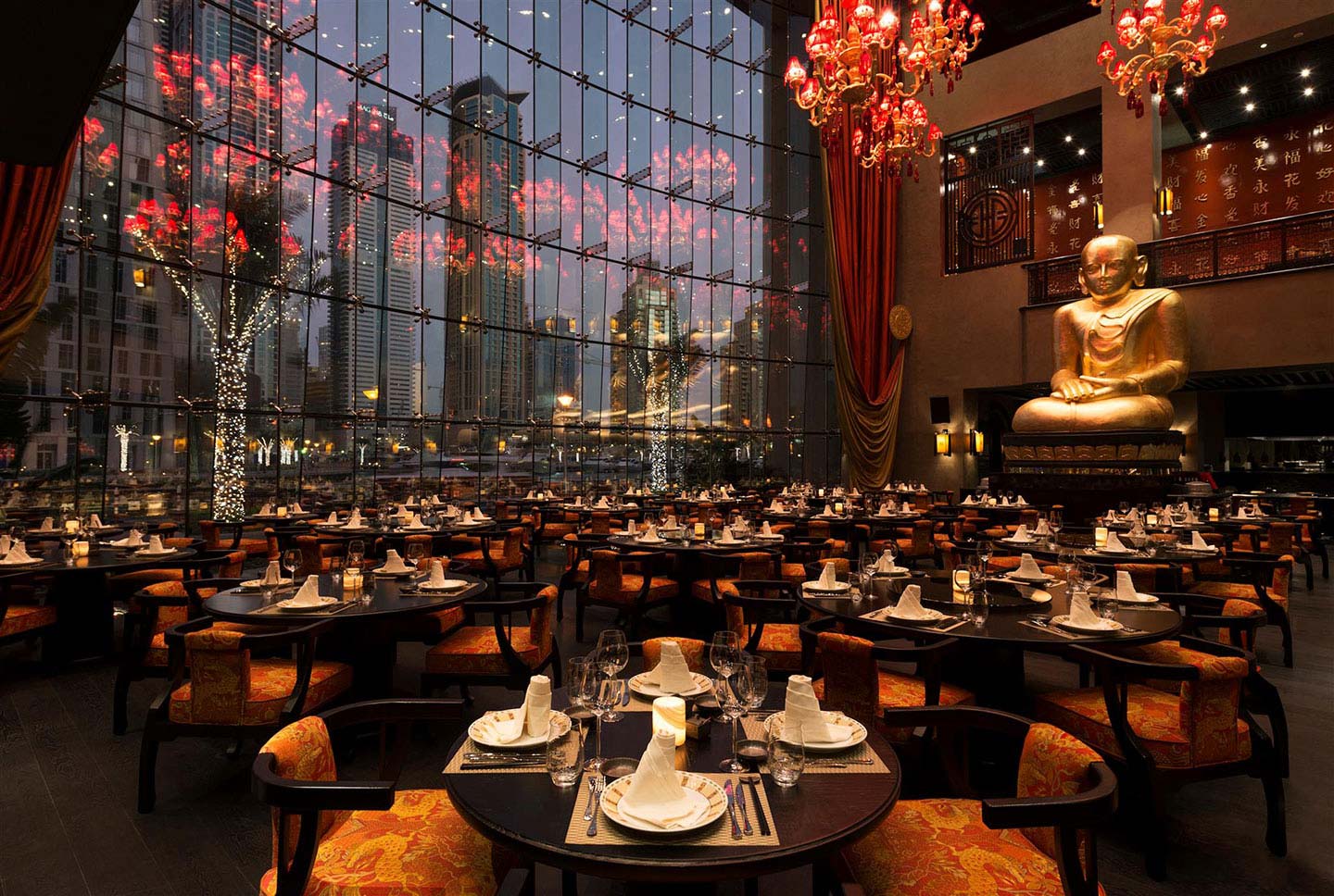The interior of the Buddha Bar restaurant in Dubai with a tall Buddha sculpture overlooking the dining tables and floor-to-window ceilings overlooking the glamorous Dubai Marina